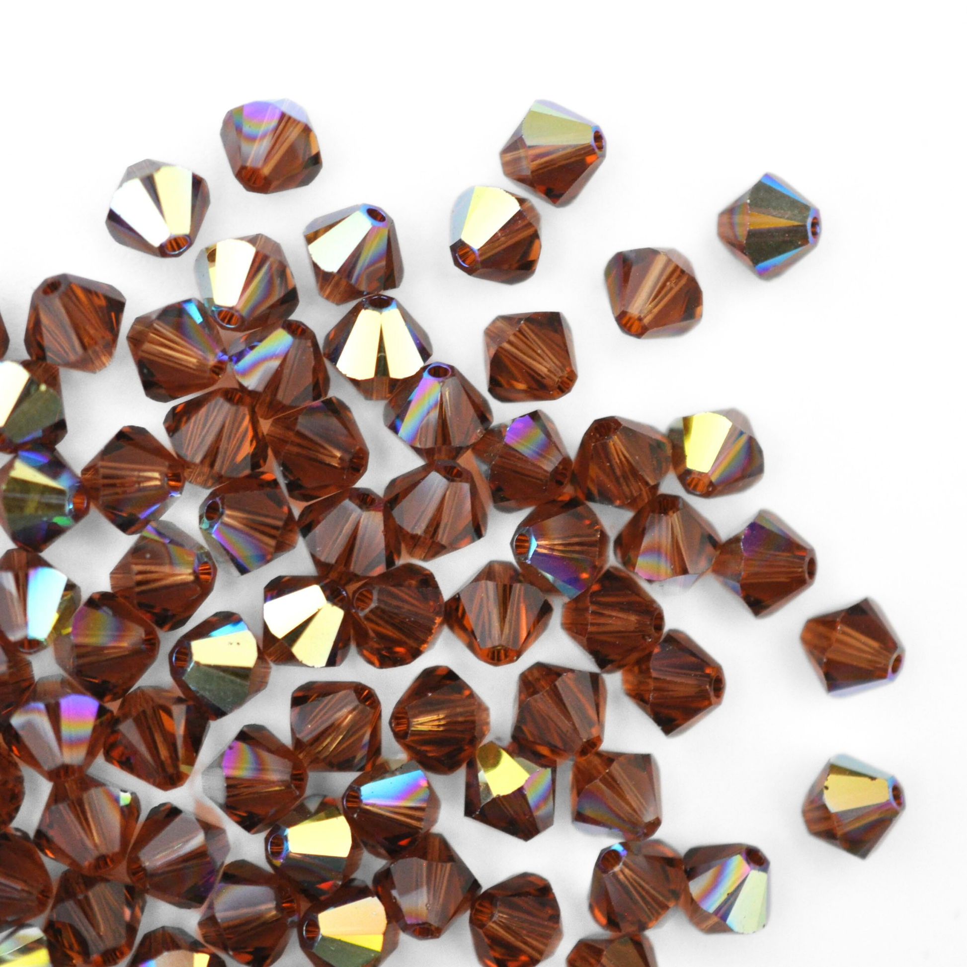 Austrian crystal 5328 bicone beads in the color Smoked Topaz AB spilling out onto a white background.