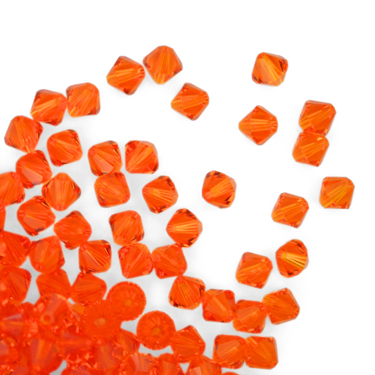Austrian crystal 5328 bicone beads in the color Tangerine spilling out onto a white background.