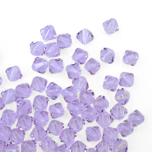 Austrian crystal 5328 bicone beads in the color Violet spilling out onto a white background.
