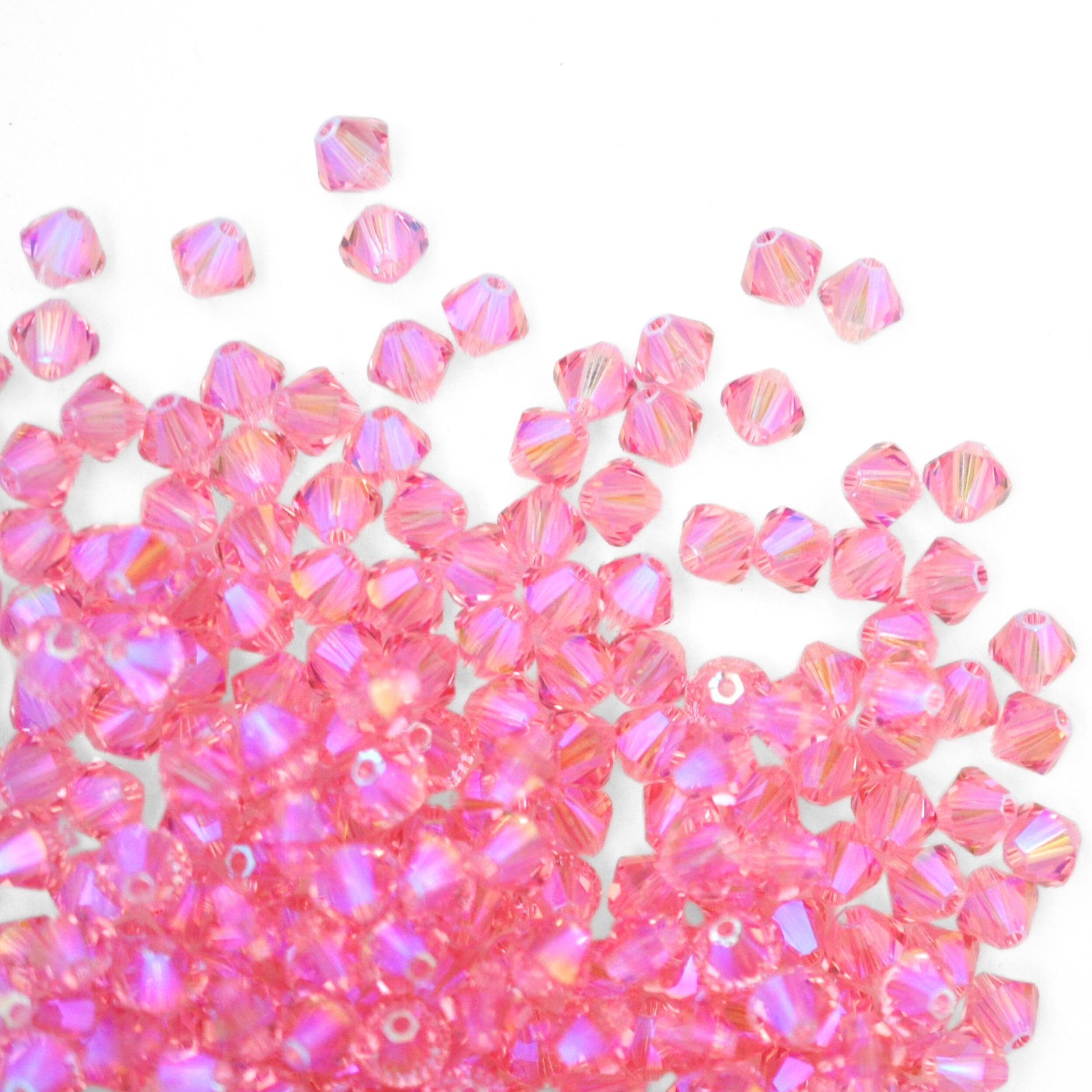Austrian crystal 5328 bicone beads in the color Light Rose Shimmer 2X spilling out onto a white background.