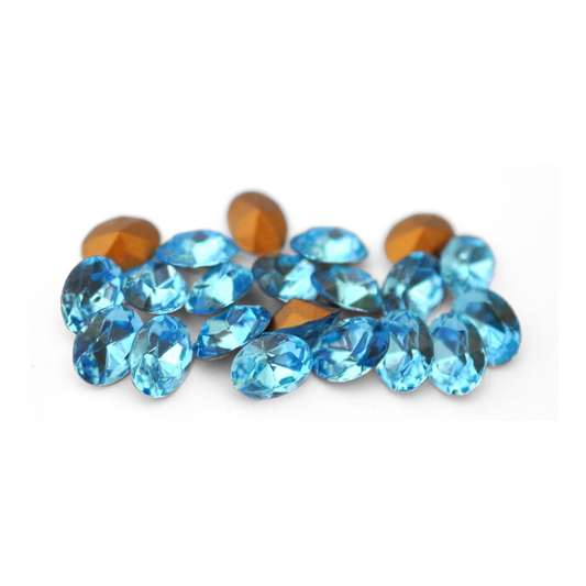 Oval shaped faceted Austrian crystal rhinestones in the color Aquamarine displayed on a white background. 