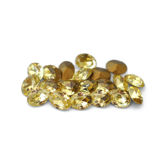 Oval shaped faceted Austrian crystal rhinestones in the color Jonquil displayed on a white background. 