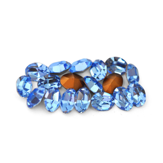 Oval shaped faceted Austrian crystal rhinestones in the color Light Sapphire displayed on a white background. 
