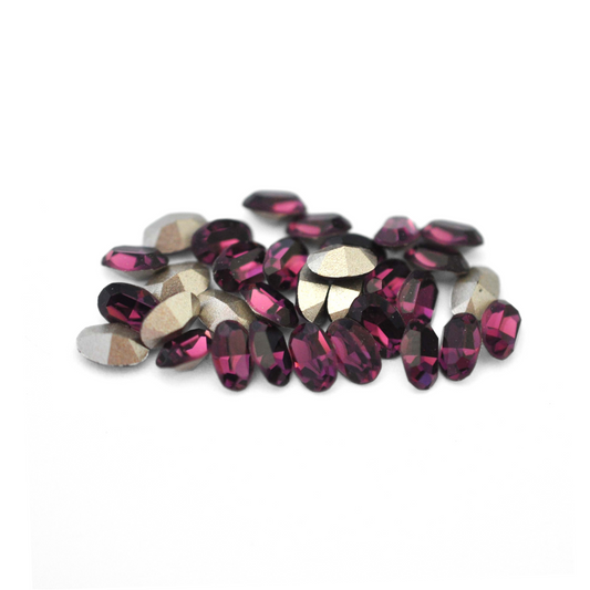 Oval shaped faceted Austrian crystal rhinestones in the color Amethyst displayed on a white background. 