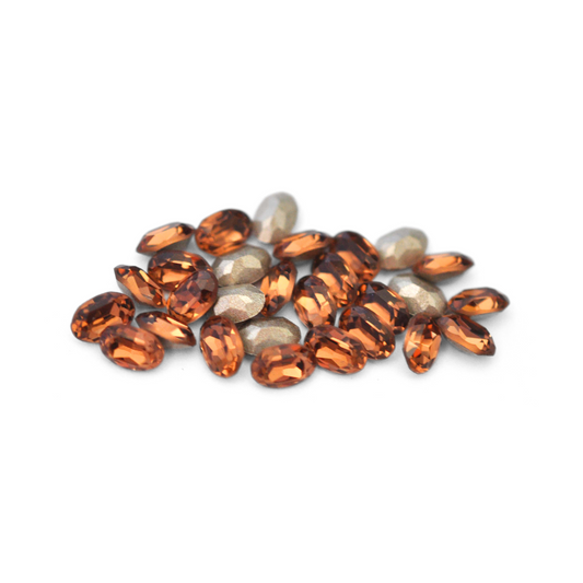 Oval shaped faceted Austrian crystal rhinestones in the color Light Smoked Topaz displayed on a white background. 