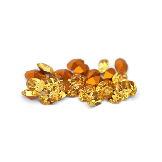 Oval shaped faceted Austrian crystal rhinestones in the color Light Topaz displayed on a white background. 