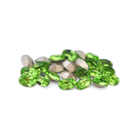 Oval shaped faceted Austrian crystal rhinestones in the color Peridot displayed on a white background. 