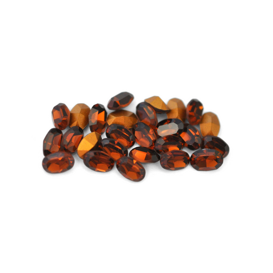 Oval shaped faceted Austrian crystal rhinestones in the color Smoked Topaz displayed on a white background. 