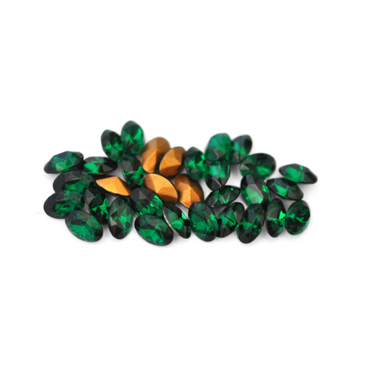 Oval shaped faceted Austrian crystal rhinestones in the color Emerald displayed on a white background. 
