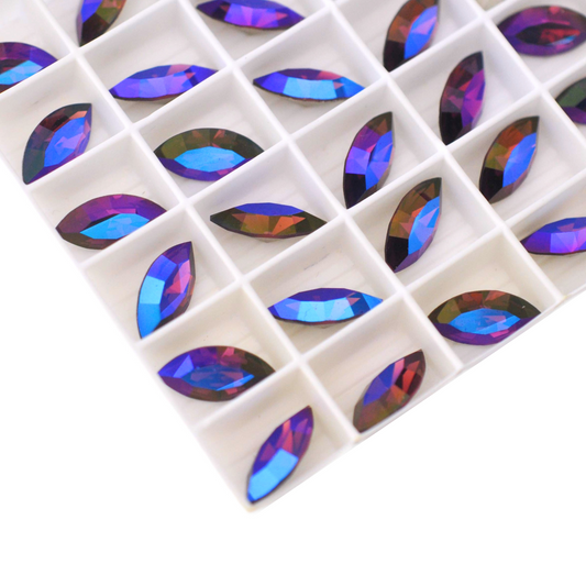 Navette shaped faceted Austrian crystal rhinestones in the color Amethyst Glacier Blue displayed in a tray on a white background.