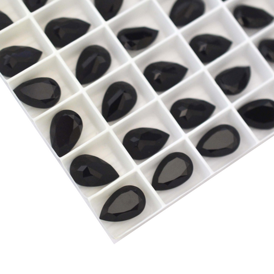 Pear shaped faceted Austrian crystal rhinestones in the color Jet displayed in the packaging tray on a white background. 