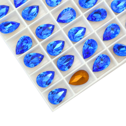 Pear shaped faceted Austrian crystal rhinestones in the color Sapphire displayed in the packaging tray on a white background. 