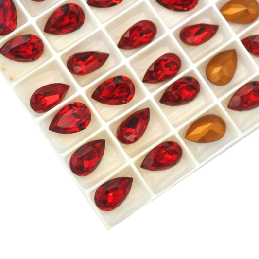 Pear shaped faceted Austrian crystal rhinestones in the color Siam displayed in the packaging tray on a white background. 