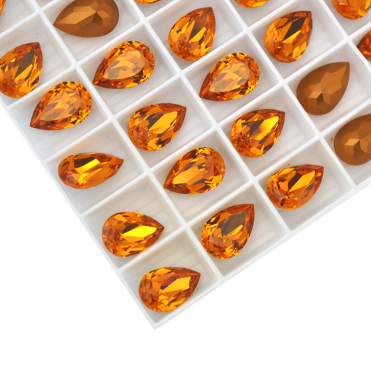 Pear shaped faceted Austrian crystal rhinestones in the color Topaz displayed in the packaging tray on a white background. 