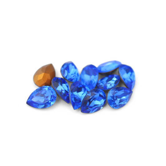 Pear shaped faceted Austrian crystal rhinestones in the color Sapphire displayed on a white background. 