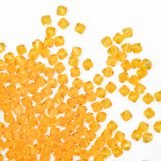 Austrian crystal 5328 bicone beads in the color Light Topaz spilling out onto a white background. 