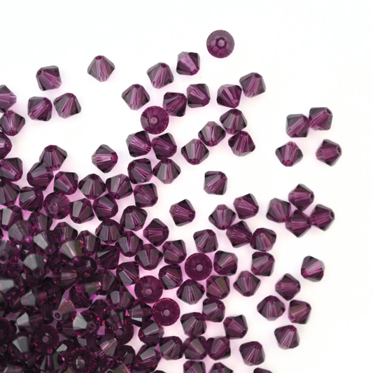 Austrian crystal 5328 bicone beads in the color Amethyst spilling out onto a white background. 