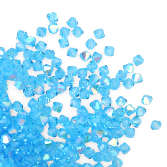 Austrian crystal 5328 bicone beads in the color Aquamarine AB spilling out onto a white background. 