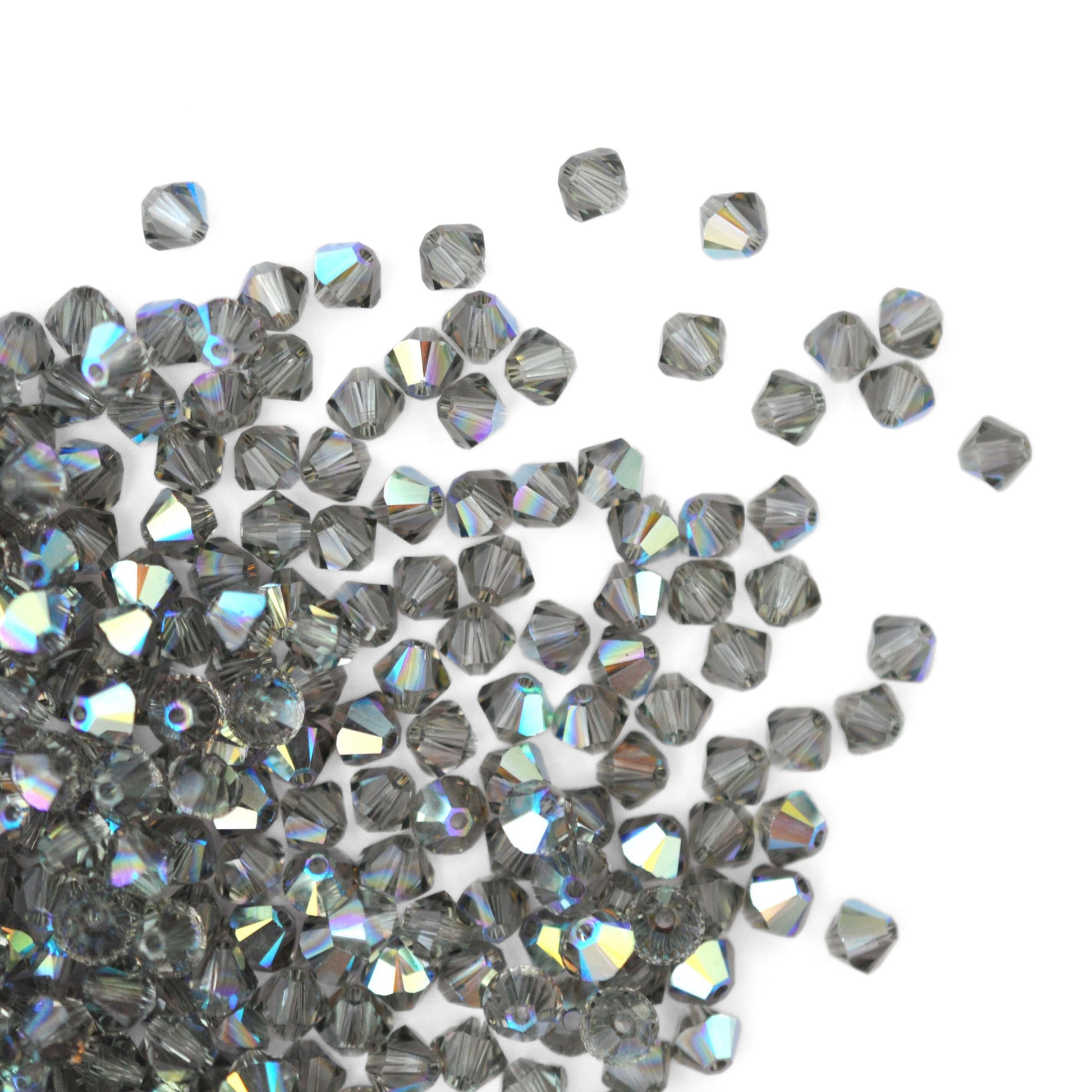 Austrian crystal 5328 bicone beads in the color Black Diamond AB spilling out onto a white background. 