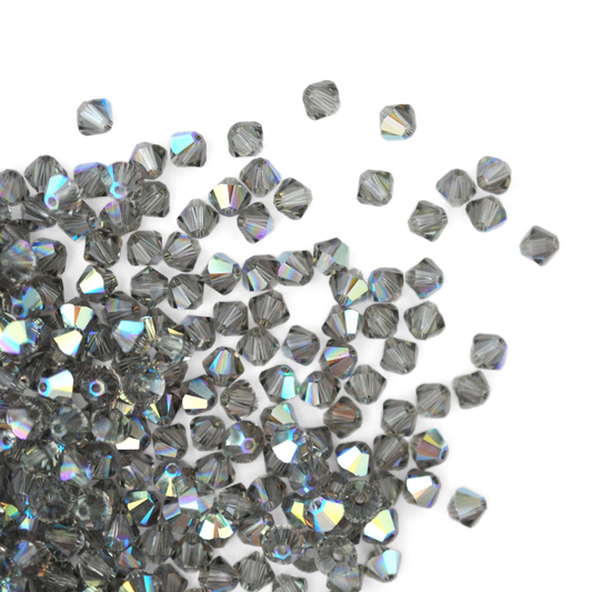 Austrian crystal 5328 bicone beads in the color Black Diamond AB spilling out onto a white background. 