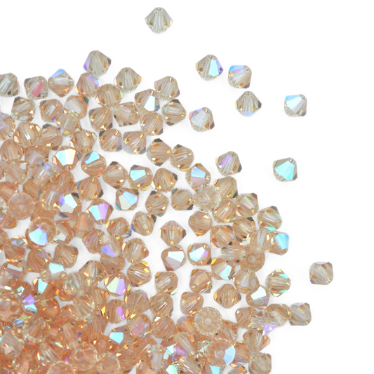 Austrian crystal 5328 bicone beads in the color Cantaloupe AB spilling out onto a white background. 