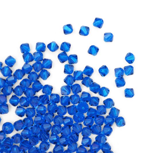 Austrian crystal 5328 bicone beads in the color Capri Blue spilling out onto a white background. 