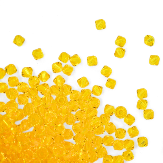Austrian crystal 5328 bicone beads in the color Citrine spilling out onto a white background. 