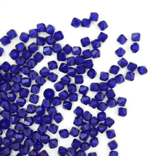 Austrian crystal 5328 bicone beads in the color Cobalt spilling out onto a white background. 