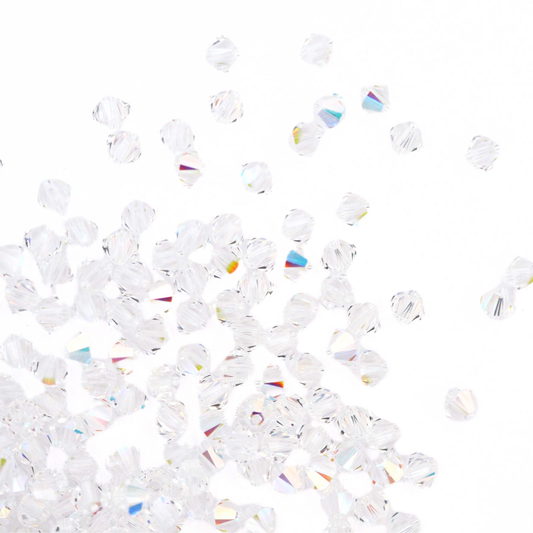 Austrian crystal 5328 bicone beads in the color Crystal AB spilling out onto a white background. 