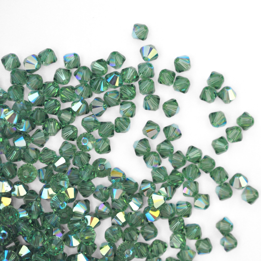 Austrian crystal 5328 bicone beads in the color Erinite AB spilling out onto a white background. 