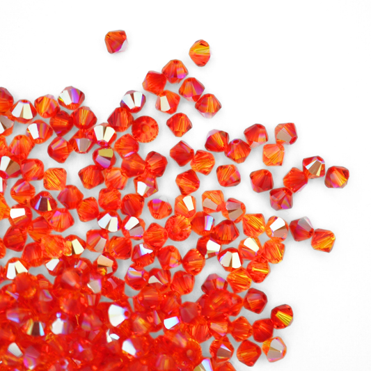 Austrian crystal 5328 bicone beads in the color Fireopal AB spilling out onto a white background. 