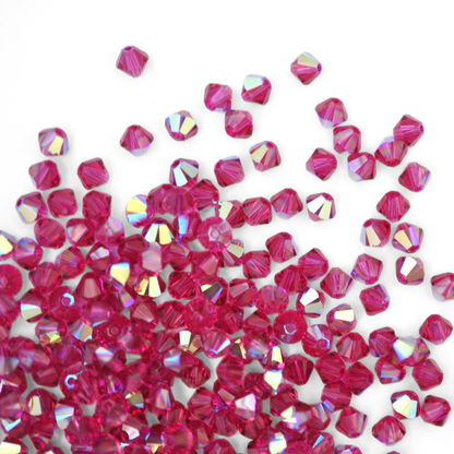 Austrian crystal 5328 bicone beads in the color Fuchsia AB spilling out onto a white background. 