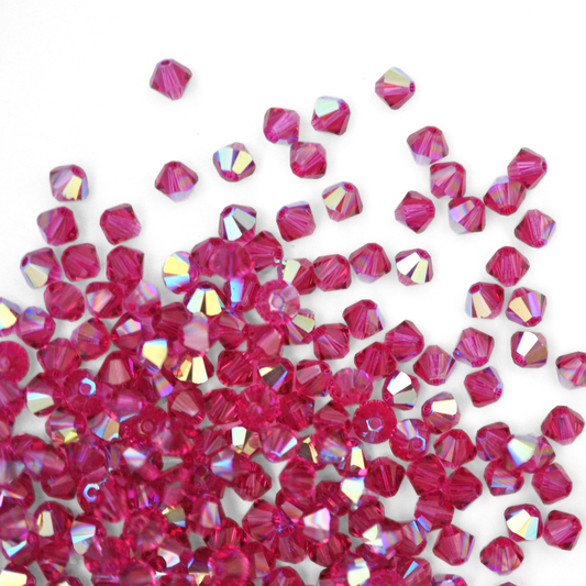 Austrian crystal 5328 bicone beads in the color Fuchsia AB spilling out onto a white background. 