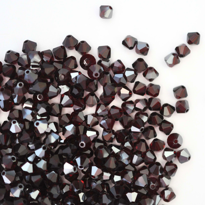 Austrian crystal 5328 bicone beads in the color Garnet Satin spilling out onto a white background. 