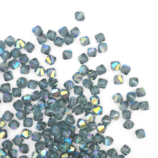 Austrian crystal 5328 bicone beads in the color Indian Sapphire AB spilling out onto a white background. 