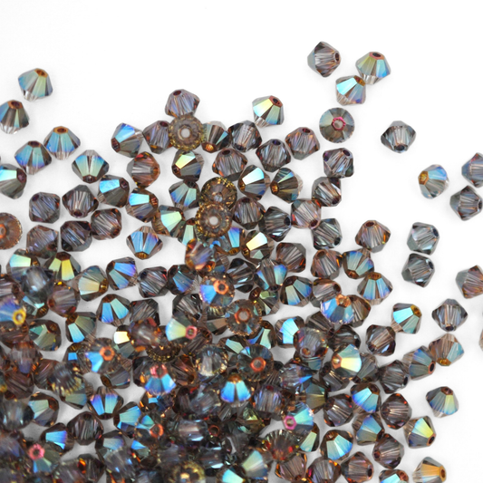 Austrian crystal 5328 bicone beads in the color Iridescent Green spilling out onto a white background. 