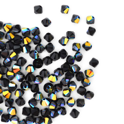 Austrian crystal 5328 bicone beads in the color Jet AB spilling out onto a white background. 