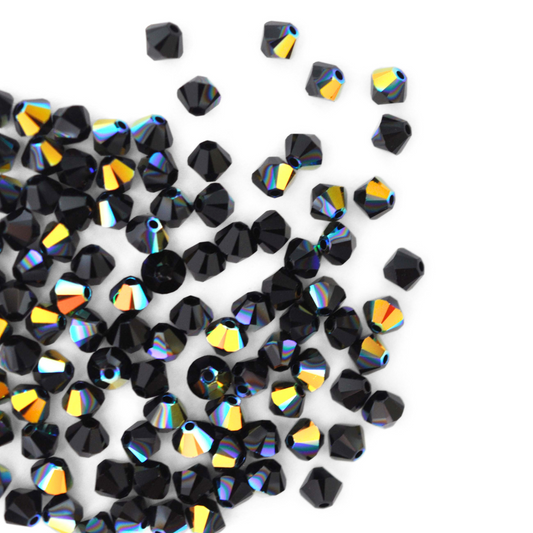 Austrian crystal 5328 bicone beads in the color Jet AB spilling out onto a white background. 