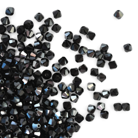 Austrian crystal 5328 bicone beads in the color Jet Hematite spilling out onto a white background. 