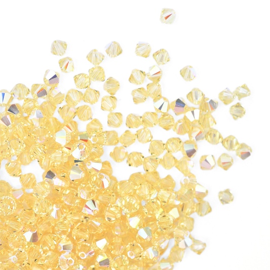 Austrian crystal 5328 bicone beads in the color Jonquil AB spilling out onto a white background. 