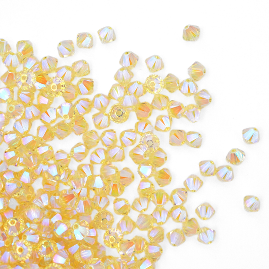 Austrian crystal 5328 bicone beads in the color Jonquil AB2X spilling out onto a white background. 