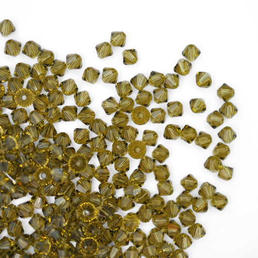 Austrian crystal 5328 bicone beads in the color Khaki spilling out onto a white background. 
