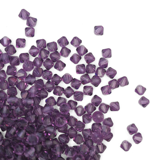 Austrian crystal 5328 bicone beads in the color Lilac spilling out onto a white background. 