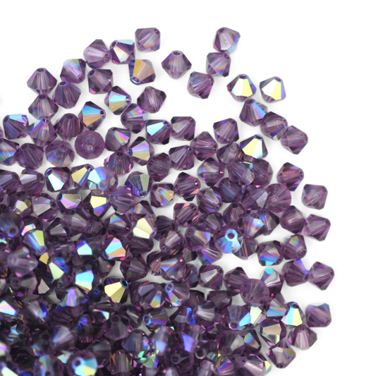 Austrian crystal 5328 bicone beads in the color Lilac AB spilling out onto a white background. 