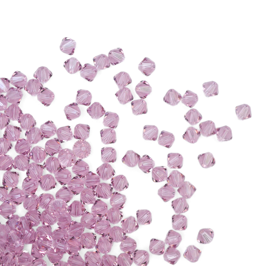 Austrian crystal 5328 bicone beads in the color Light Amethyst spilling out onto a white background. 