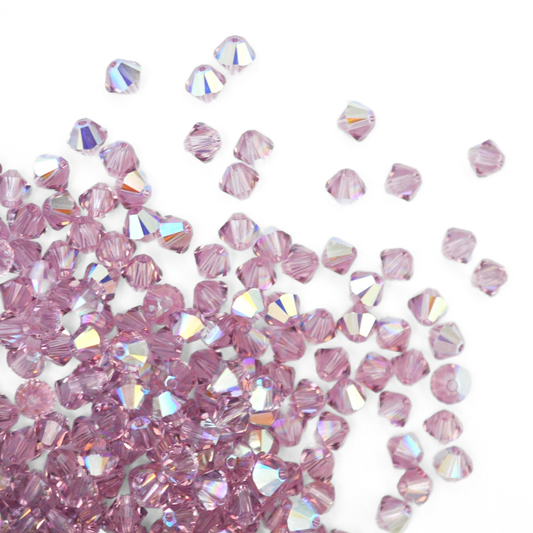 Austrian crystal 5328 bicone beads in the color Light Amethyst AB spilling out onto a white background. 