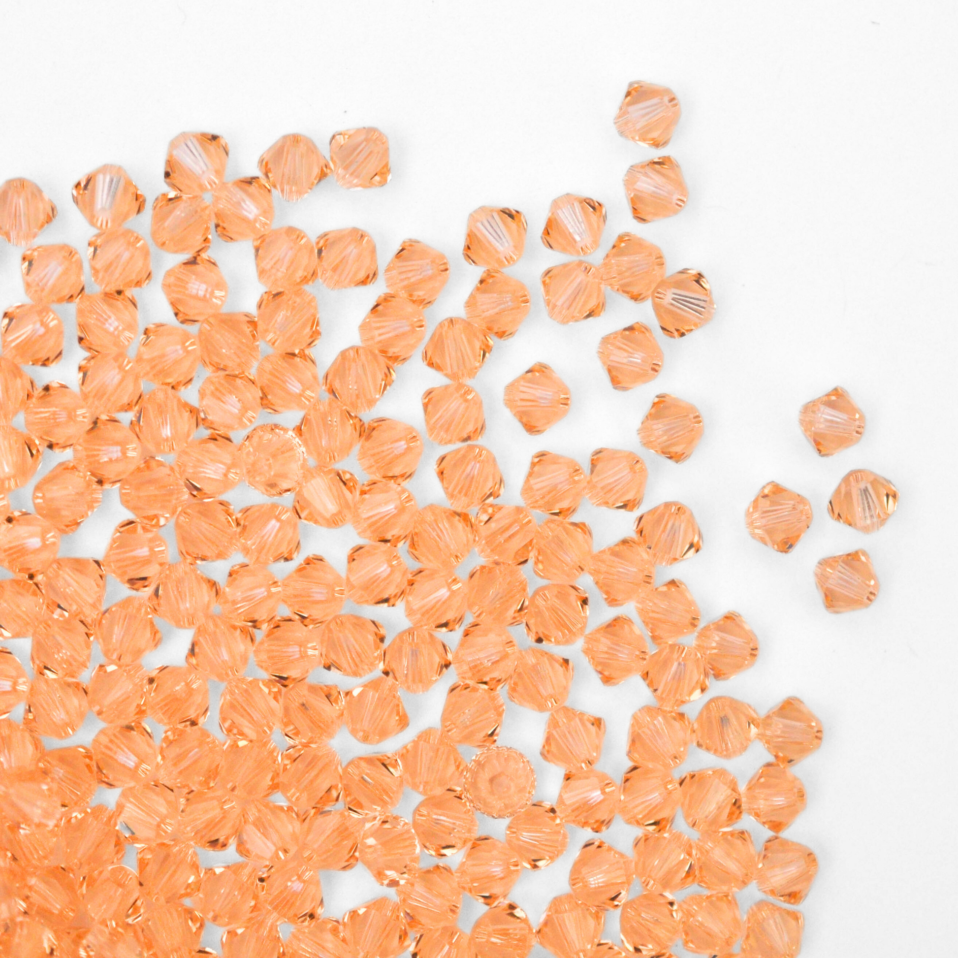 Austrian crystal 5328 bicone beads in the color Light Peach spilling out onto a white background. 