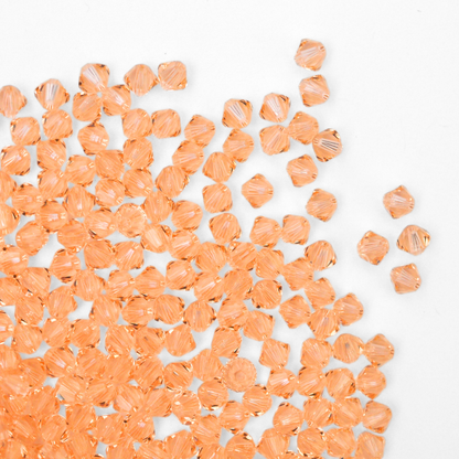 Austrian crystal 5328 bicone beads in the color Light Peach spilling out onto a white background. 
