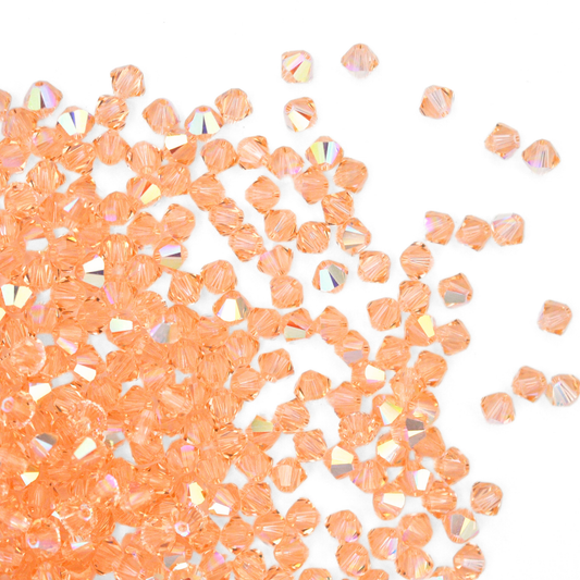 Austrian crystal 5328 bicone beads in the color Light Peach AB spilling out onto a white background. 