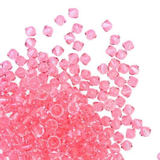 Austrian crystal 5328 bicone beads in the color Light Rose spilling out onto a white background. 